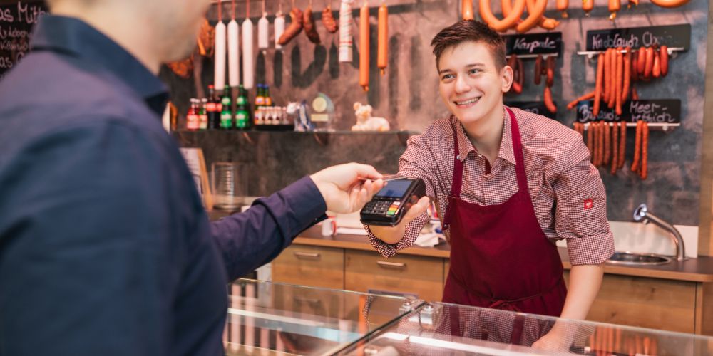 Verkäufer eine Metzgerei hält das EC-Terminal von POS-cashservice über den Tresen damit ein Kunde bezahlen kann.
